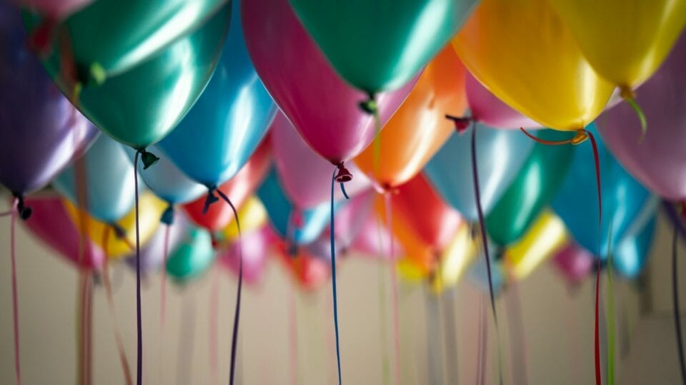 A ceiling filled with colorful balloons, including yellow, pink, blue, green, and purple, floating with their ribbons hanging down.